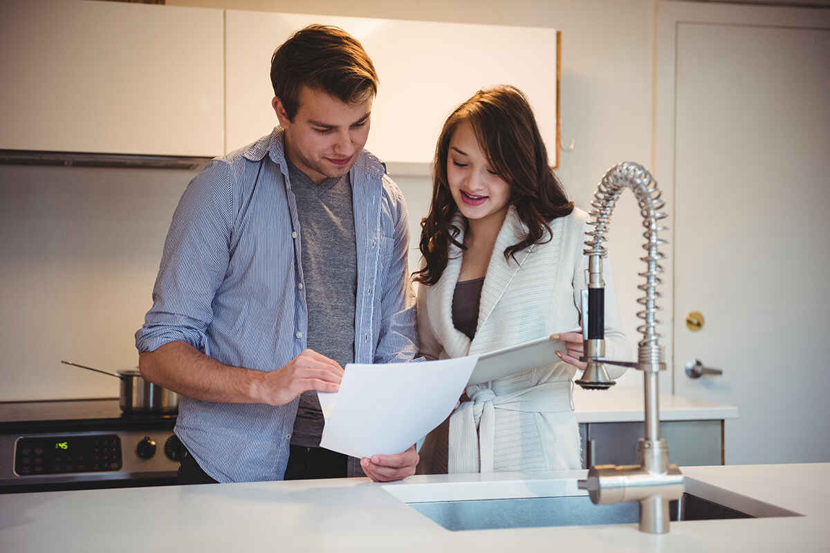 A couple reviewing a high water bill together in their kitchen near a sink faucet.