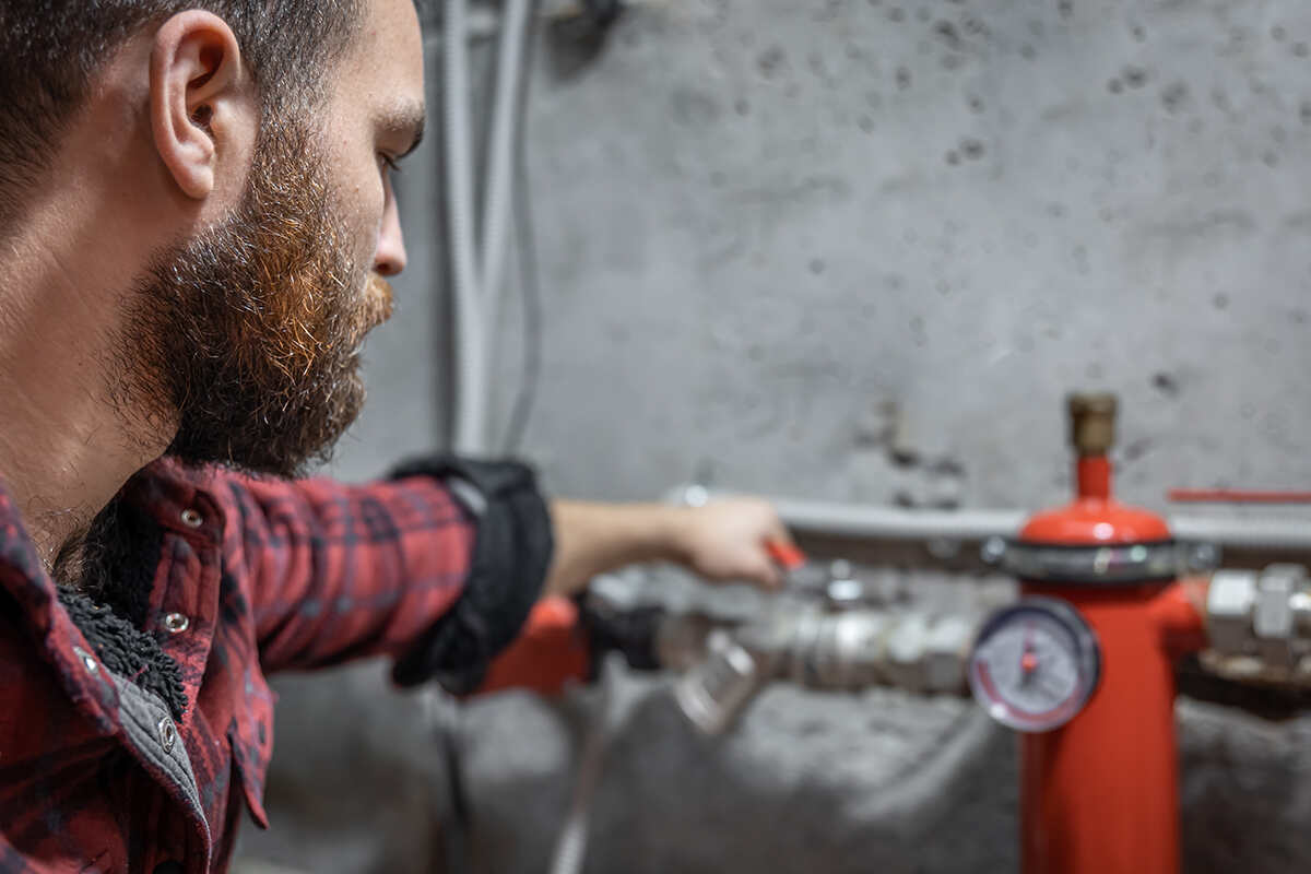 A plumber in a plaid shirt calibrating a water pressure regulator system by tuning its adjustment valve.